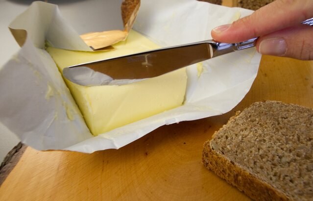 Person schneidet Stück Butter mit Buttermesser ab | © Land schafft Leben
