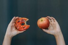 Hände, die einen Donut und einen Apfel halten | © Pexels