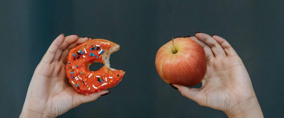 Hände, die einen Donut und einen Apfel halten | © Pexels
