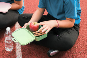 Kind sitzt mit Jausenbox mit Knäckebrot und Apfel auf der Laufbahn | © Land schafft Leben