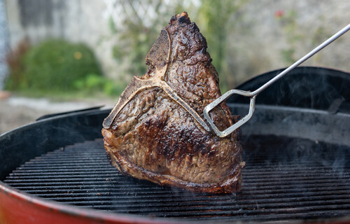 Zange hält Rindsteak über Grillrost | © Land schafft Leben