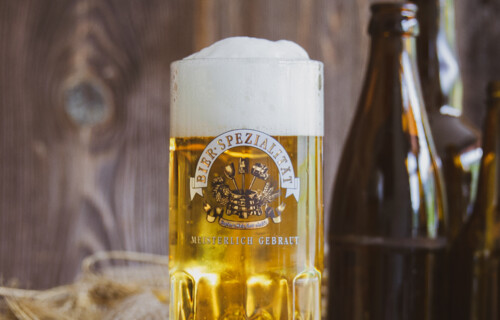 Bierspezialität | © Land schafft Leben Volle Bierglas auf Holztisch mit braunen Bierflaschen im Hintergrund | © Land schafft Leben