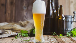 Volles Weißbierglas vor dunklen Flaschen auf Holztisch | © Land schafft Leben