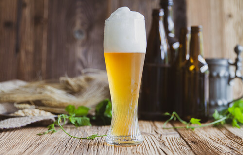 Volles Weißbierglas vor dunklen Flaschen auf Holztisch | © Land schafft Leben