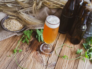 Volles Bierglas auf Holztisch neben mehreren dunklen Bierflaschen | © Land schafft Leben