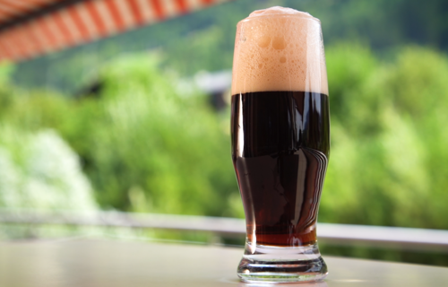 Mit dunklem Bier vollgefülltes Glas auf Balkon | © Land schafft Leben