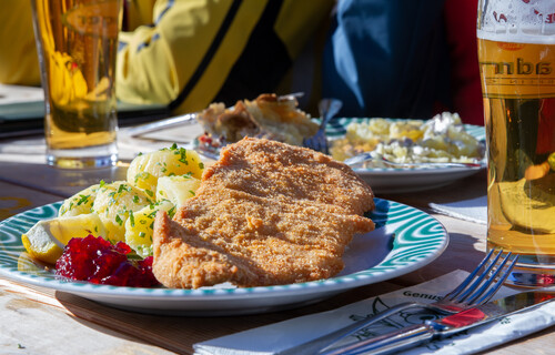 Teller mit Wiener Schnitzel und Kartoffeln neben Bierglas auf Tisch | © Land schafft Leben