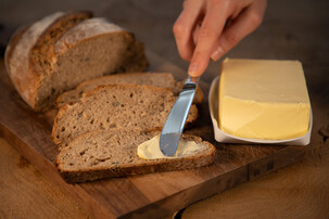 Person streicht Butter auf Schwarzbrot | © Land schafft Leben