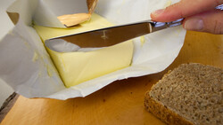 Person schneidet Stück Butter mit Buttermesser ab | © Land schafft Leben