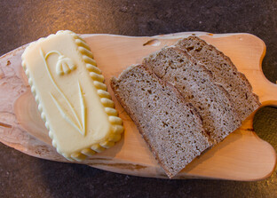 Verziertes Stück Butter liegt neben Schwarzbrot auf Holzbrett | © Land schafft Leben