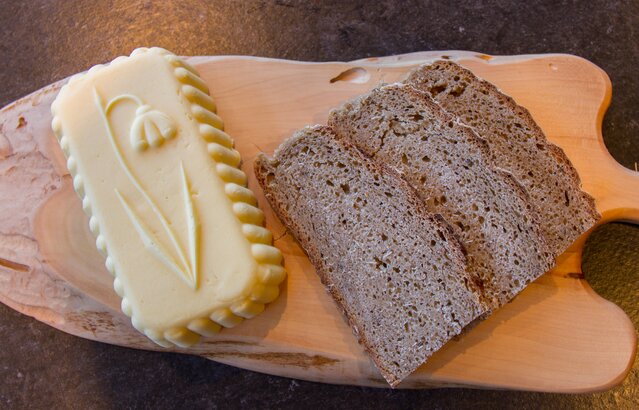 Verziertes Stück Butter liegt neben Schwarzbrot auf Holzbrett | © Land schafft Leben