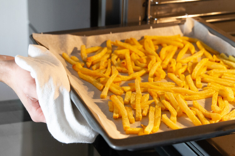 Person zieht mit Geschirrtuch Blech mit Pommes aus Rohr | © Land schafft Leben