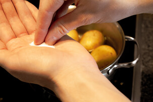 Hand mit Salzhaufen vor Kochtopf mit Kartoffeln | © Land schafft Leben