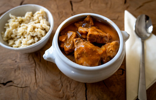 Gulasch im Teller auf Tisch neben Nockerl | © Land schafft Leben