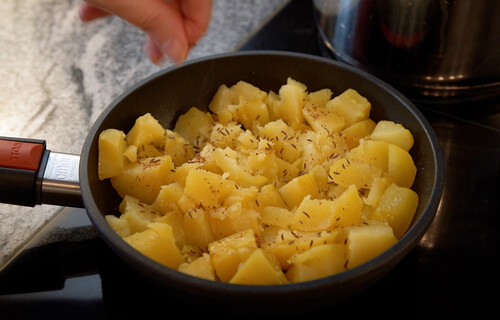 Hand würzt Kartoffeln in Pfanne | © Land schafft Leben