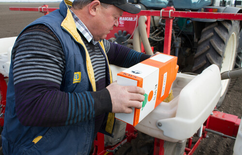 Mann füllt Saatgut in Behälter hinter Traktor | © Land schafft Leben