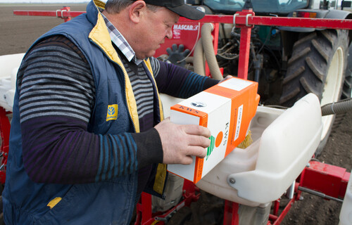 Mann füllt Saatgut in Behälter hinter Traktor | © Land schafft Leben